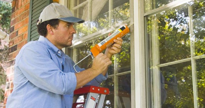 man on ladder caulking window