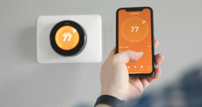 person holding smart phone in front of smart thermostat