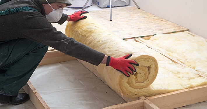 person wearing gloves while rolling out insulation