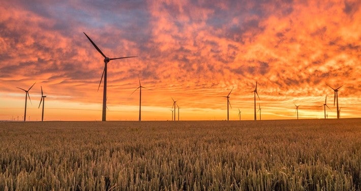 Wind turbines in a flat field against a vibrant sunset