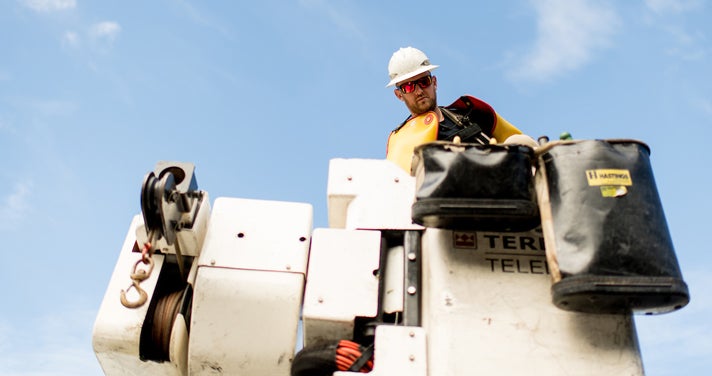 Lineworker looking down from a bucket against a blue sky