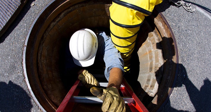 utility worker climbing down hole in street to repair underground wires