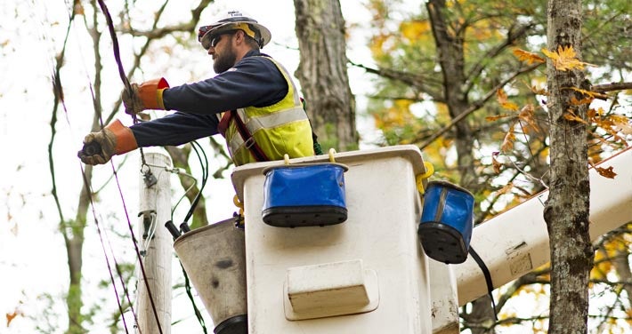 closeup of lineworker fixing utility line with tress in background