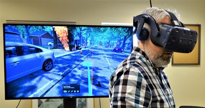 Unitil employee with virtual reality goggles stands in front of simulator