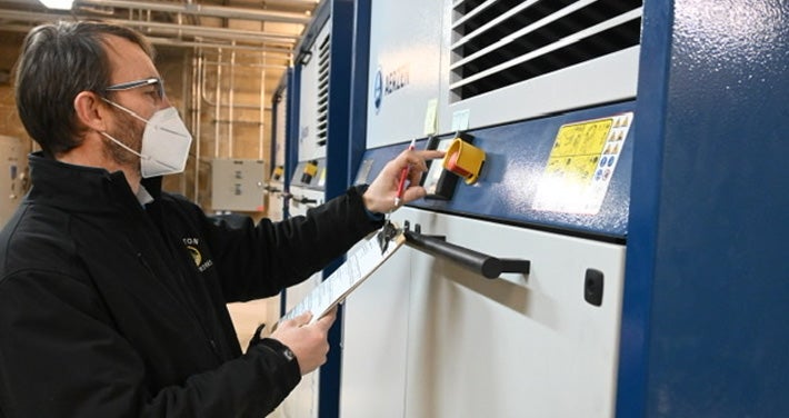 a wastewater plant employee stands with clipboard in front of new machine