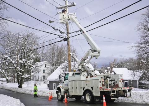 Unitil bucket truck with worker fixing powerline on snowy street